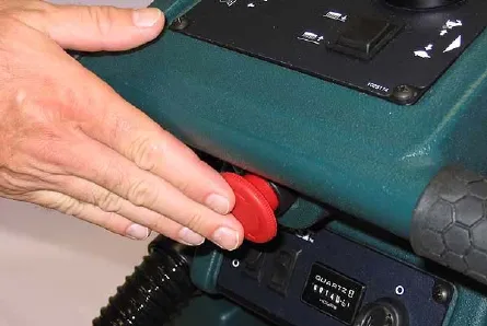 Hand striking the red emergency stop button on the control console