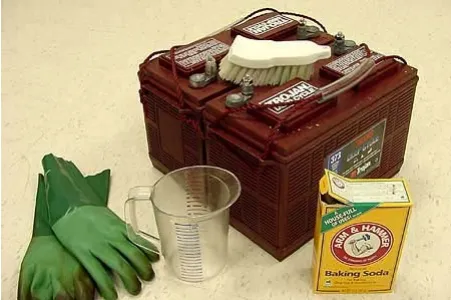 Batteries with a scrub brush, a measuring cup, a box of baking soda and rubber gloves