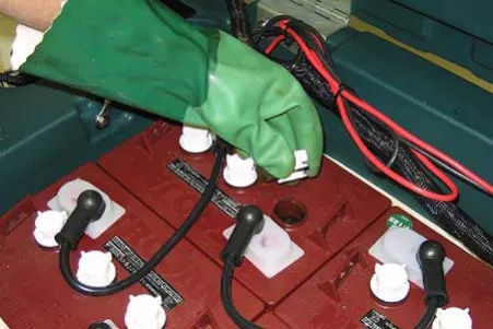 Gloved hand checking the fluid level in a battery cell