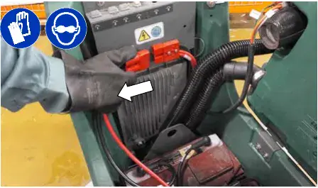 Hand pulling apart the battery cable connection at the machine, arrow marking the connector