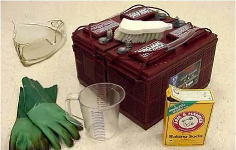 Battery cleaning supplies: safety glasses, gloves, scrub brush, measuring cup and baking soda beside a battery