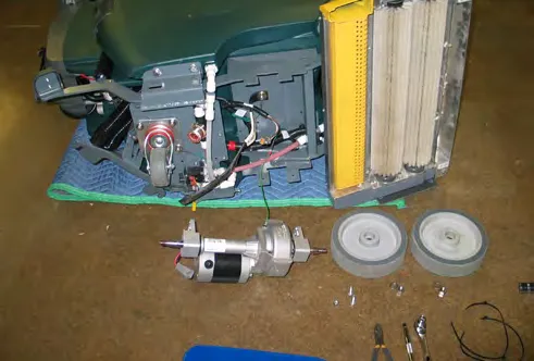 Machine on its side with the transaxle motor and both wheels removed and laid on the floor