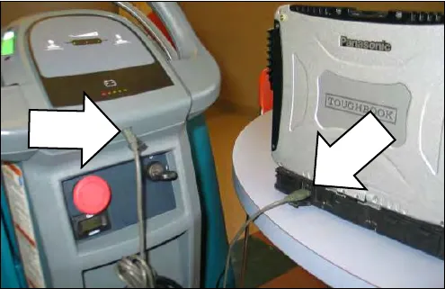 Photo of a notebook computer connected by USB cable to the external port on the machine control console, with arrows pointing at the machine port and the notebook port
