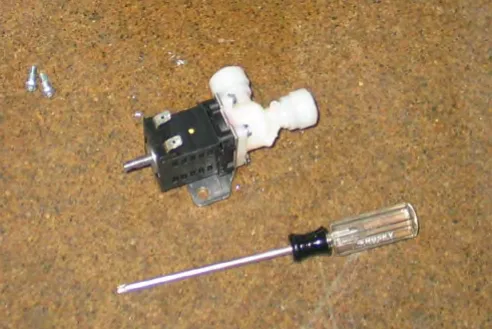 Water solenoid removed and lying on the floor beside a screwdriver and two screws