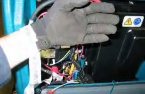 Gloved hand with a static wrist strap attached near the battery negative terminal