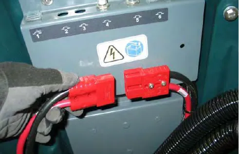 Gloved hand disconnecting the red battery connectors