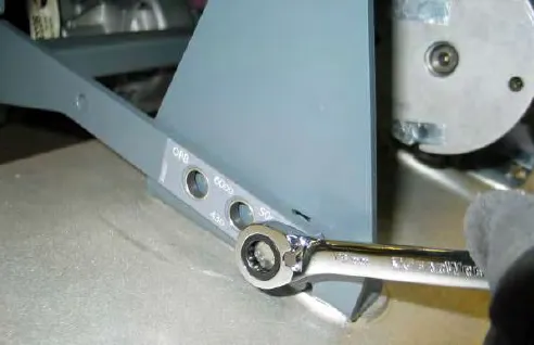 Removing a lift mechanism mounting bolt with a ratchet wrench, with hole selection marks on the lift arm visible