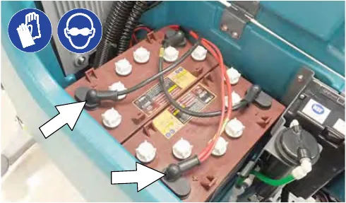 Two arrows pointing at the battery cable connections on the batteries, with glove and eye protection symbols