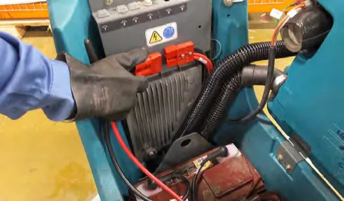 Gloved hand disconnecting the red battery connectors