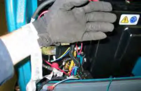 Gloved hand with a static wrist strap attached near the battery negative terminal