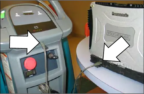 Photo of a notebook computer connected by USB cable to the external port on the machine control console, with arrows pointing at the machine port and the notebook port