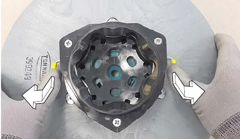 Hands pressing the yellow spring clips down and outward on the pad driver