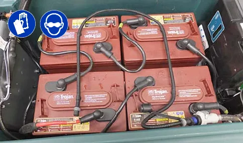Four batteries in the compartment with the watering system hoses; protective gloves and eye protection symbols