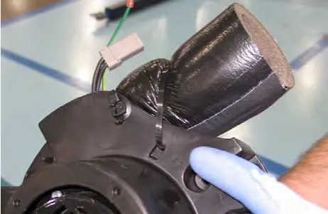 Gloved hand at the cable tie holding the exhaust muffler to the vacuum fan mount
