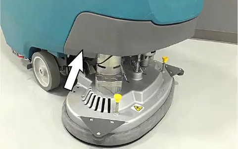 Arrow pointing to the area behind the front scrub head cover where the drain cap is located