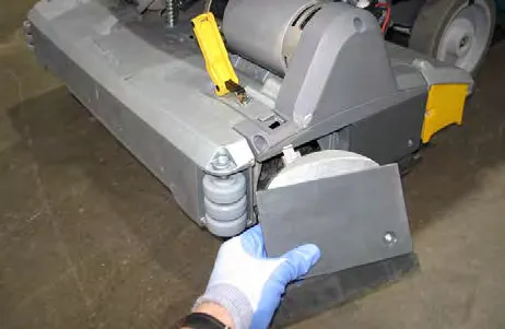 Hand unfastening the yellow latch on the idler plate at the side of the scrub head