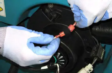 Gloved hands cutting the zip tie on the vacuum fan wire connections
