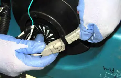Gloved hands disconnecting the main wire harness from the vacuum fan
