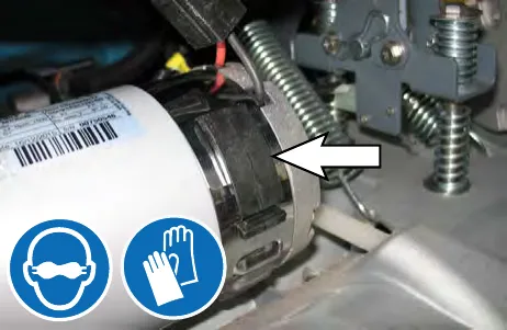Arrow pointing to the latch on the retaining band of the cylindrical brush motor; safety glasses and gloves symbols shown