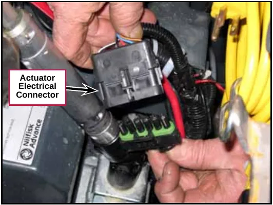Hands separating the actuator electrical connector, a black housing with a green mating connector, near the yellow cord. Label: Actuator Electrical Connector.