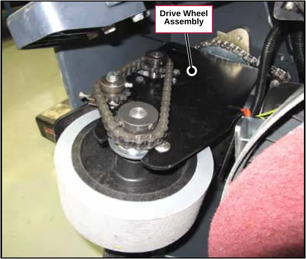 Photo of the drive wheel assembly under the front of the machine, with the machine lying on its side, showing the drive wheel, chain and sprockets