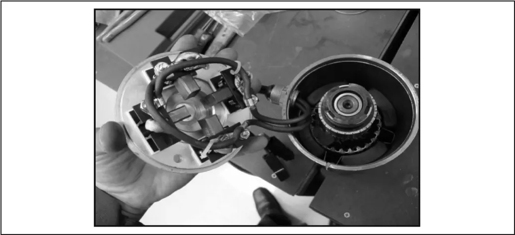 Photo of the removed top cover held in a hand beside the motor housing, showing the four carbon brush holders