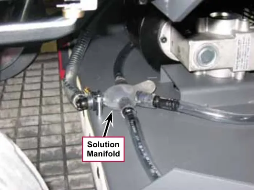 Photo of the solution manifold, a clear plastic tee fitting joining hoses, with a callout and arrow labeled Solution Manifold