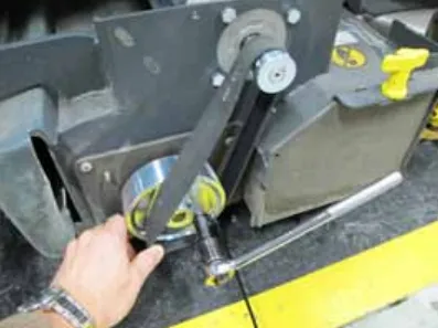 Photo of a hand holding the belt over the small pulley while a ratchet turns the large pulley to roll the belt on