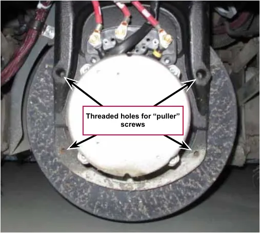 Photo of the front drive wheel with the motor facing forward; four arrows point to the threaded holes for the puller screws in the casting around the motor