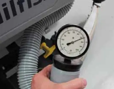 Photo of a hand holding the vacuum water lift gauge against the end of the vacuum hose on the machine