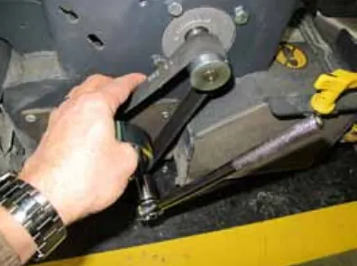 Photo of a hand pulling the belt outward while a ratchet turns the large pulley to roll the belt off
