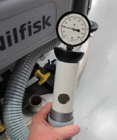 Photo of a hand holding the vacuum gauge on top of a white pipe open-hole adapter that has a round hole in its side, attached to the hose end