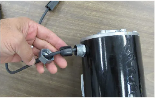 Photo of a hand holding the wire retaining nut and rubber packing removed from the motor cable entry.