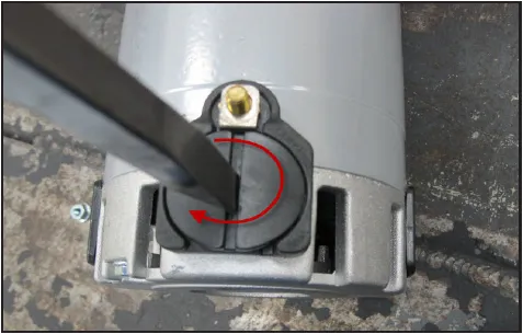 Photo of a slotted screwdriver turning the brush cap, with a red arrow showing the turning direction.