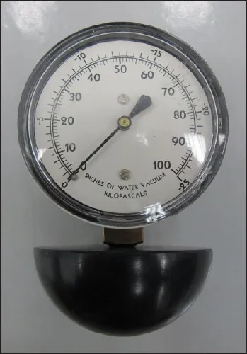 Water lift gauge: a round dial gauge marked in inches of water vacuum and kilopascals, mounted on a black rubber cup