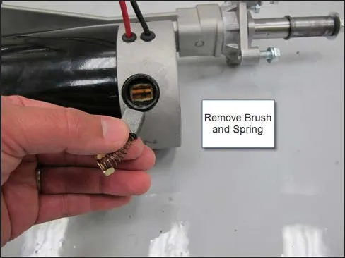 Photo of a hand pulling a carbon brush and spring out of the transaxle motor, labeled Remove Brush and Spring