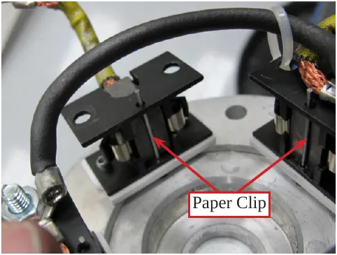 Photo of the brush holders with paper clips through the holes in front of the brushes, two arrows labeled Paper Clip.