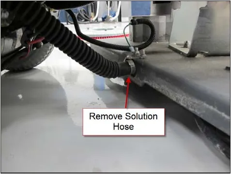 Photo of the solution hose and its clamp at the brush head, with an arrow and the label Remove Solution Hose.