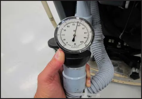 Hand holding the vacuum gauge against the end of the vacuum hose, with the needle visible on the dial