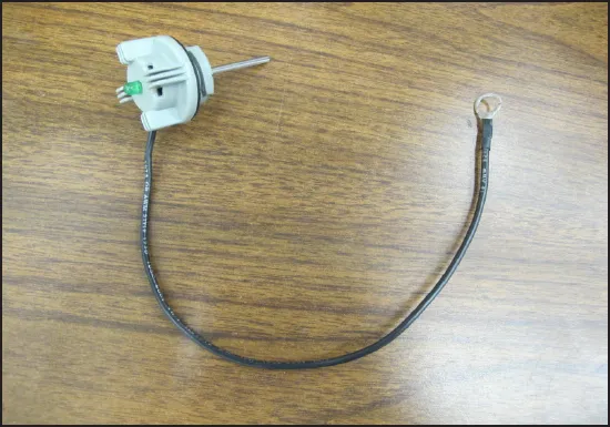 Battery fill indicator on a wood bench: a gray fill cap with a green LED and a black wire lead ending in a ring terminal