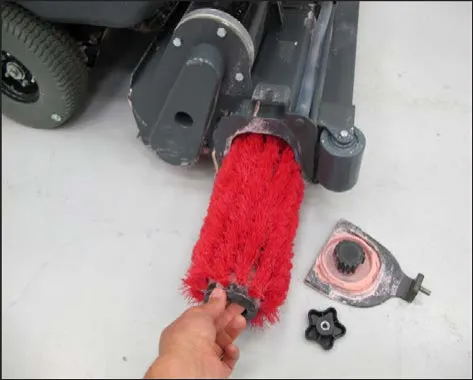 A hand pulling the red cylindrical brush out of the brush housing