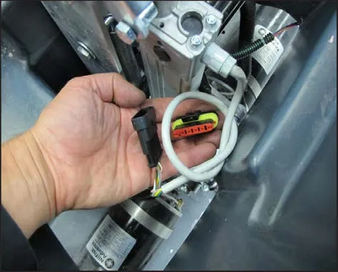 A hand holding the disconnected actuator electrical connector, with the actuator above it