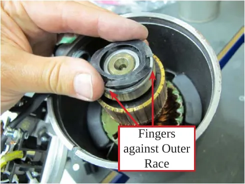 Hand holding the spring washer over the motor armature, with arrows from the label “Fingers against Outer Race” to the washer fingers