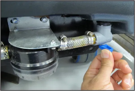 Photo under the machine showing a hand at the blue lever of the shut off valve beside the solution filter