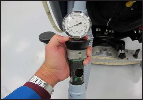 Hand holding the vacuum gauge on top of a one inch open-hole adapter fitted to the hose end, with the needle visible on the dial