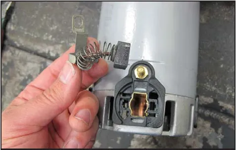 Photo of the removed carbon brush with its spring beside the empty brush holder.