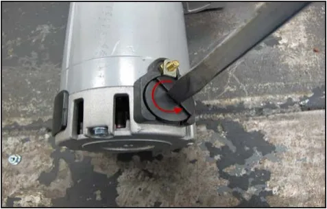 Photo of a motor end with a large slotted screwdriver in the round plastic brush cap and a red arrow showing the turning direction.