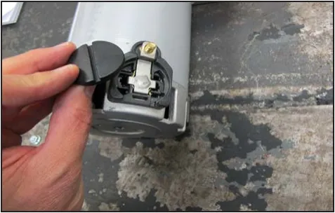 Photo of a hand lifting the round plastic brush cap off the motor, exposing the brush holder.