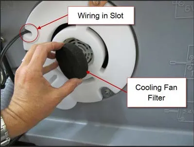 Hand installing the round black foam cooling fan filter in the vacuum motor cover, with arrows from the labels “Wiring in Slot” to the slot in the cover and “Cooling Fan Filter” to the filter