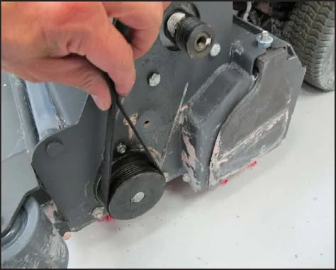 A hand fitting the belt over the brush drive pulley at the brush head side plate